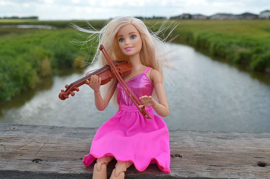 barbie tocando el gesto del violín en el muelle de madera marrón